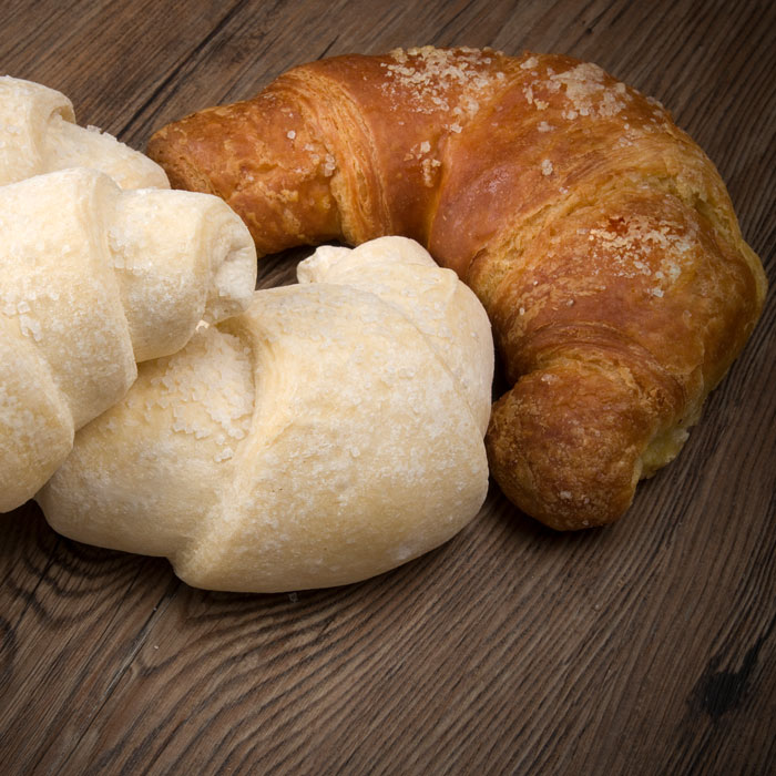 Zwei Croissant-Teiglinge und ein fertiges Croissant/Two croissant dough pieces and one baked croissant