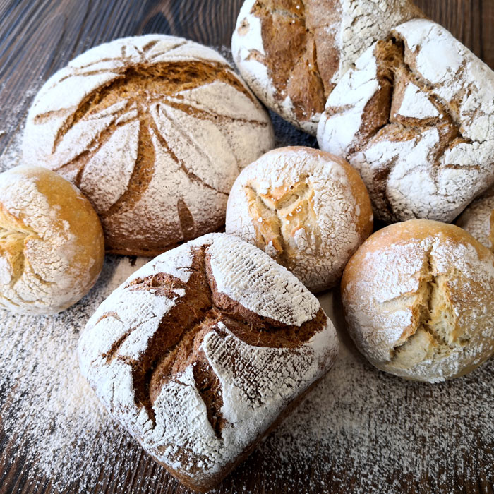 Verschiedene helle und dunklere Brötchen und Brote, mehlbestäubt/Various light and dark rolls and breads, dusted with flour